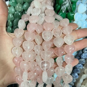 May include: A strand of pink and clear heart-shaped gemstone beads. The beads are translucent and have a natural, polished finish.