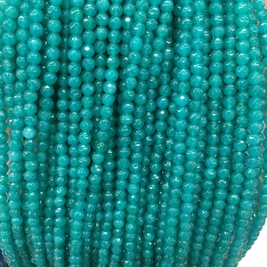 May include: A strand of teal green faceted gemstone beads. The beads are round and have a smooth, polished finish.