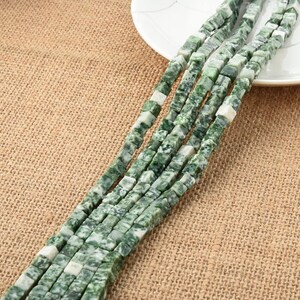 Puede incluir: Una hebra de cuentas cuadradas verdes y blancas hechas de piedra natural. Las cuentas están enhebradas en un hilo transparente y están listas para ser utilizadas para la elaboración de joyas.