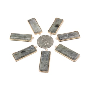 Peut inclure: Sept pendentifs en pierre de labradorite à bordure dorée, chacun avec une boucle pour attacher une chaîne. Les pendentifs sont disposés en étoile autour d'une pièce de 25 cents américaine.