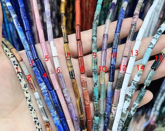 May include: Assortment of 15 different types of gemstone beads, each strand featuring a unique color and pattern. The beads are all cylindrical in shape and are arranged in a row on a hand.