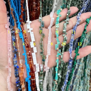 Op de afbeelding: Twaalf strengen edelsteen kralen, elk met een andere kleur en patroon. De kralen zijn vierkant en hebben een ruwe, natuurlijke textuur. De strengen zijn in een rij gerangschikt, met de nummers 1 tot en met 12 naast elke streng.