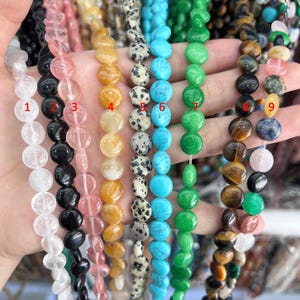May include: A close-up of ten strands of beads, each with a different color and pattern. The beads are round and smooth, and they are strung on a clear thread. The beads are arranged in a row, and they are all about the same size. The beads are made of various materials, including gemstone, glass, and plastic.