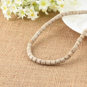 May include: A strand of off-white round beads made of natural stone. The beads are strung on a clear thread and are arranged in a circular pattern. The beads are lying on a brown burlap surface.