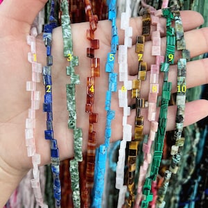 Puede incluir: Diez hebras de cuentas de piedras preciosas de forma cuadrada, cada hebra de un color diferente. Las cuentas están dispuestas en fila, con los colores de izquierda a derecha: blanco, azul, verde, rojo, turquesa, blanco, marrón, rosa, verde y verde.