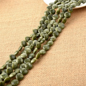 May include: A strand of green gemstone beads, each bead is round and flat, with a speckled pattern. The beads are arranged in a line on a brown burlap background.