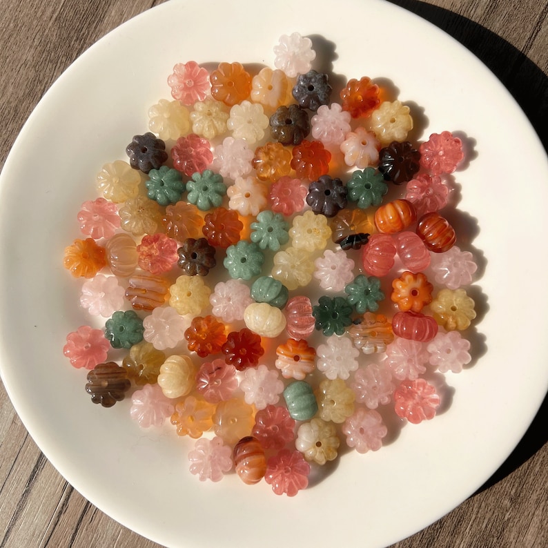 May include: A collection of colorful flower-shaped beads made of various types of stone. The beads are in shades of green, pink, orange, and brown.