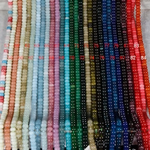 Könnte beinhalten: Eine Sammlung von Perlenketten in verschiedenen Farben, darunter Rosa, Blau, Grün und Orange. Jede Halskette besteht aus kleinen, runden Perlen und wird in einer vertikalen Reihe präsentiert. Die Perlen sind von 57 bis 84 nummeriert.