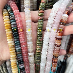 Peut inclure: Plusieurs rangées de perles de pierres précieuses de différentes couleurs, dont le jaune, le vert, le rose, le blanc et le marron. Les perles sont rondes et plates, en forme de disque. Huit rangées de perles sont visibles.