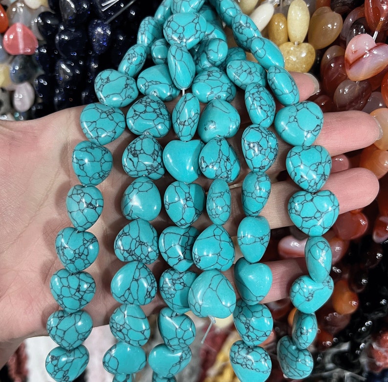May include: A strand of turquoise heart-shaped beads. The beads are a light blue color with dark blue veining. The beads are strung on a clear elastic cord.