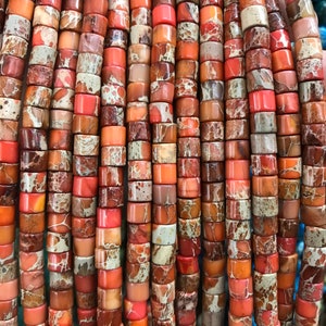 Puede incluir: Una hebra de cuentas de piedras preciosas de color naranja, marrón y blanco. Las cuentas son redondas y tienen un patrón de mármol.