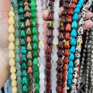 May include: Twelve strands of gemstone beads, each strand featuring a different type of stone. The beads are teardrop shaped and strung on a cord. The stones include yellow, green, white, red, blue, and black.
