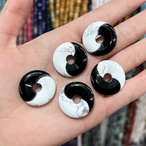 May include: Five black and white yin yang stone beads with a hole in the center. The beads are round and have a smooth, polished finish.