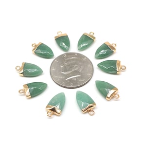 Puede incluir: Diez colgantes de punta de flecha de piedra verde con detalles dorados. Los colgantes están dispuestos en círculo alrededor de una moneda de dólar estadounidense.