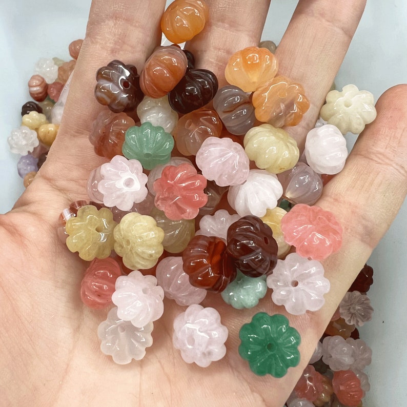 May include: Assortment of colorful gemstone beads in various shades of pink, green, brown, and white. The beads are carved in a flower shape with a hole in the center for stringing.