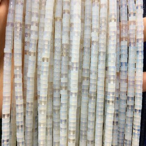 May include: A strand of white opal beads with a square shape. The beads are strung on a clear thread and have a slight iridescent sheen.