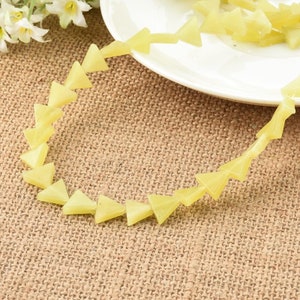 May include: A strand of pale yellow triangle-shaped beads. The beads are strung together on a clear thread. The beads are arranged in a circular pattern.