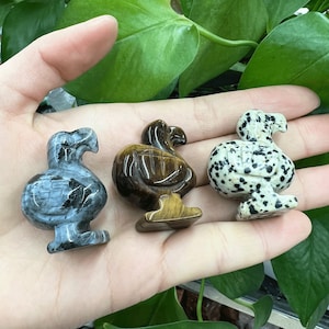 May include: Three carved dodo bird figurines made of different types of stone. The first is a gray and black stone, the second is a brown and gold tiger's eye stone, and the third is a white and black dalmatian jasper stone.