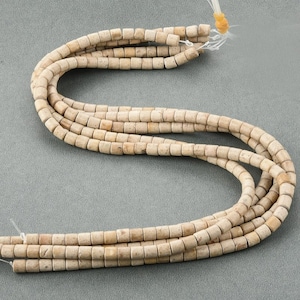 May include: A strand of light beige, cylindrical beads made of fossilized coral. The beads are approximately 1/2 inch in diameter and have a rough, textured surface.