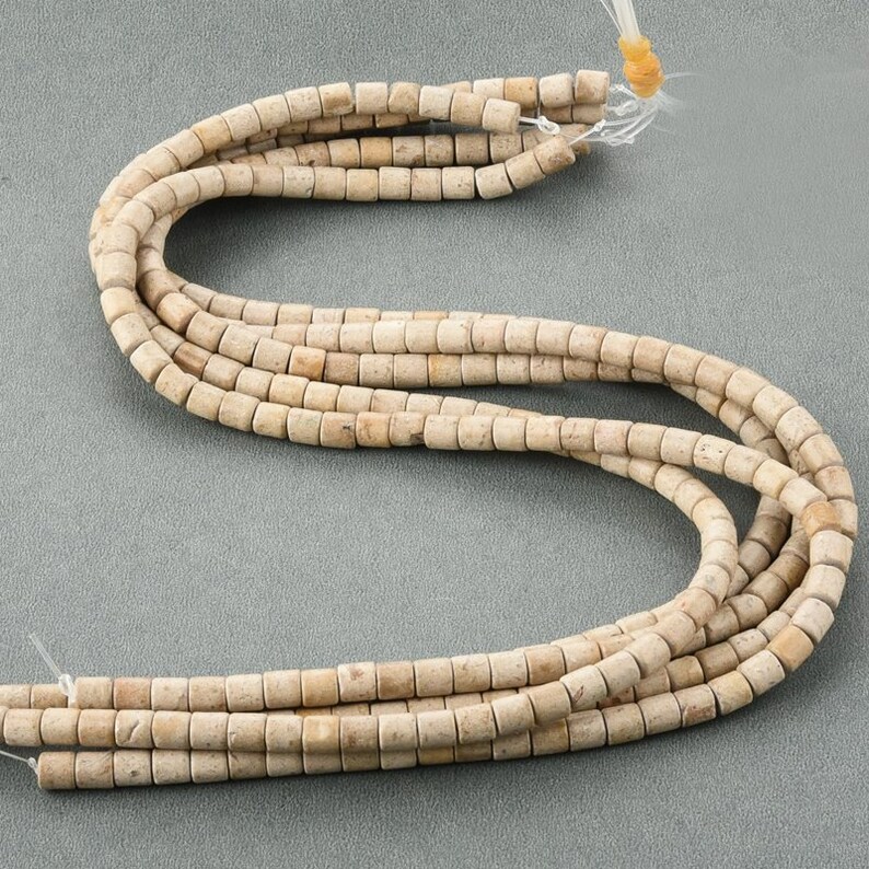 May include: A strand of light beige, cylindrical beads made of fossilized coral. The beads are approximately 1/2 inch in diameter and have a rough, textured surface.