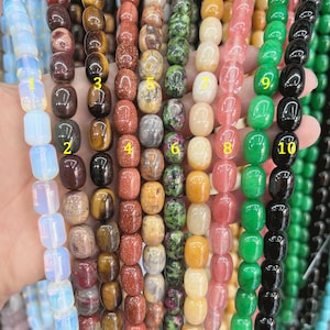 Puede incluir: Diez hebras de cuentas de piedras preciosas, cada hebra es de un color y tipo de piedra diferente. Las hebras están dispuestas en fila, de izquierda a derecha, los colores son: blanco, rojo, marrón, naranja, beige, verde, amarillo, rosa, verde y negro.