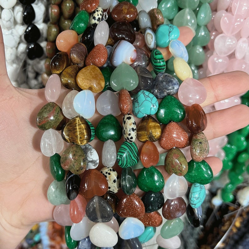 May include: A collection of heart-shaped gemstone beads in various colors, including green, brown, pink, and white. The beads are strung together on a string and are ready to be used for jewelry making.