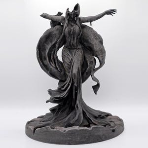 May include: A dark grey sculpture of a figure with outstretched arms and flowing robes. The statue has a detailed texture and is mounted on a circular base. The figure's head is tilted back, and the drapery creates a sense of movement.