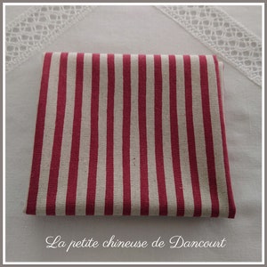 Peut inclure: Tissu rayé rouge et blanc plié sur une surface blanche. Le tissu a une texture tissée. Le texte "La petite chineuse de Dancourt" est imprimé sous le tissu.