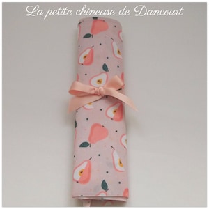 Può includere: Un rotolo di tessuto rosa con un motivo a pera pesca e un nastro rosa legato intorno. Il tessuto ha uno sfondo bianco con punti neri. Il testo "La petite chinoise de Dancourt" è stampato nella parte superiore dell'immagine.