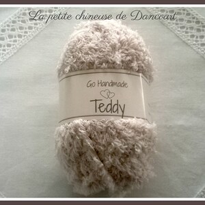 Puede incluir: Un ovillo de hilo beige con la etiqueta "Go Handmade Teddy" para tejer o hacer ganchillo.
