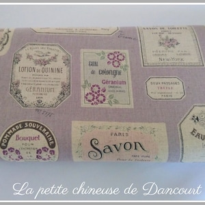 Peut inclure: Un tissu lavande avec un motif répété d'étiquettes de style vintage. Les étiquettes présentent des motifs floraux et du texte en français, notamment "Eau de Cologne", "Savon" et "Lotion de Quinine".