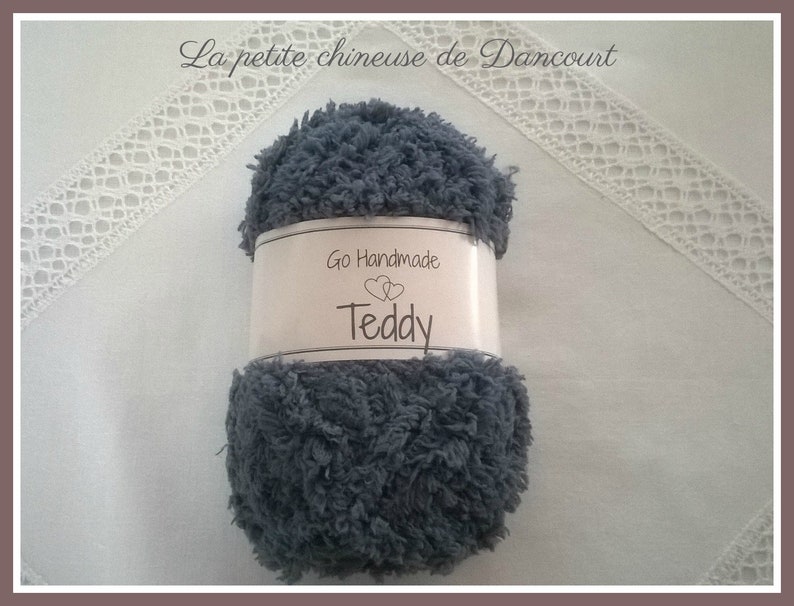 Puede incluir: Un ovillo de hilo gris con la etiqueta "Go Handmade Teddy" para tejer o hacer ganchillo.