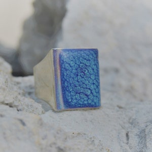 Può includere: Un anello d'argento con una pietra rettangolare blu. La pietra ha una superficie testurizzata.