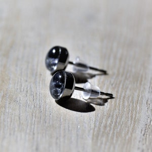 May include: A pair of small, round, black stud earrings with silver posts.