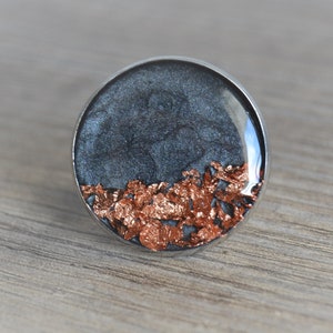 May include: A round resin ring with a dark gray base and copper flakes embedded in the resin.