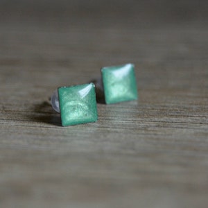 May include: A pair of square-shaped earrings with a metallic green finish.