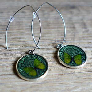 May include: A pair of silver dangle earrings with green butterfly charms. The butterflies are encased in clear resin and have a green and gold color scheme.