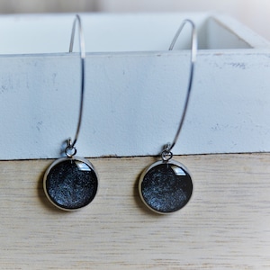 May include: A pair of silver hoop earrings with black round pendants. The pendants have a sparkly, glittery finish.