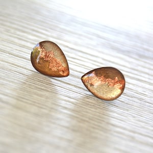 Peut inclure: Une paire de boucles d'oreilles en forme de goutte avec une finition métallique dorée et cuivrée.