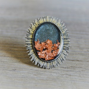 Könnte beinhalten: Ein silberner Ring mit einem runden Design, das eine blaue und kupferfarbene Harz-Einlage aufweist.