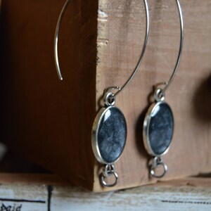 May include: A pair of silver hoop earrings with black and white resin cabochons. The earrings are hanging from a wooden surface.