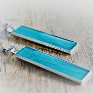 May include: A pair of turquoise blue rectangular dangle earrings with silver metal hooks.