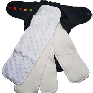 May include: A black cloth diaper with colorful snaps and several white absorbent inserts. One insert has a textured, dotted surface. The inserts are various sizes and shapes, designed to fit inside the diaper.