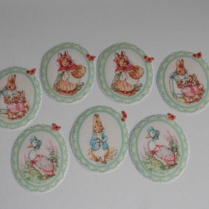 May include: A set of seven oval-shaped fabric patches featuring illustrations of rabbits and ducks in various outfits. Each patch has a scalloped light green border and a small red butterfly accent on the edge, showcasing classic storybook characters.