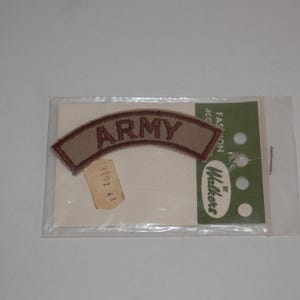 May include: A curved, tan embroidered patch with the word ARMY stitched in brown thread. The patch is enclosed in a clear plastic sleeve attached to a white backing card featuring the text FASHION ACCESSORIES BY WALKERS and a small price tag.