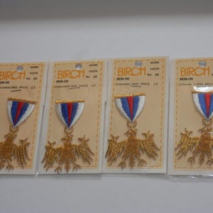 May include: Four identical Birch brand iron-on embroidered patches on individual cardboard backing cards. Each patch features a gold eagle emblem suspended from a white, blue, and red striped ribbon motif. The packaging includes the text BIRCH.