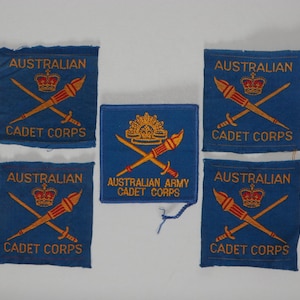 May include: Five square blue fabric patches with embroidered gold text and imagery. Four patches feature the text AUSTRALIAN CADET CORPS with a crown and crossed torches. One central patch features the text AUSTRALIAN ARMY CADET CORPS.