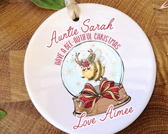 May include: White ceramic Christmas ornament with a bee in a snow globe. The ornament reads "Auntie Sarah Have a Bee-autiful Christmas Love Aimee".