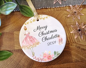 May include: White ceramic Christmas bauble featuring a ballerina illustration, gold glitter, pink flowers, and the text "Merry Christmas Charlotte 2021".