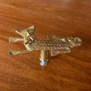 以下が含まれることがあります： テクスチャ加工された表面を持つ、スタイリッシュな動物の形をした金色のドアノブ。ノブは丸いベースを持ち、ドアに取り付けられています。